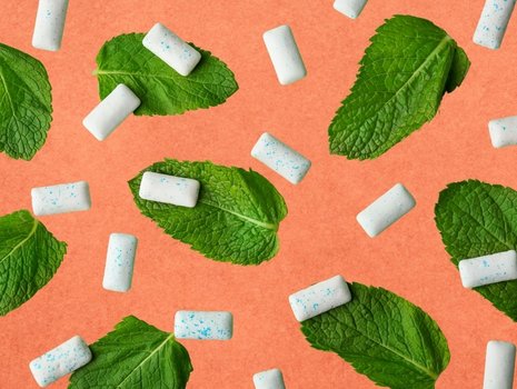 Kaugummi-Dragees neben Pfefferminzblättern auf orangenem Hintergrund