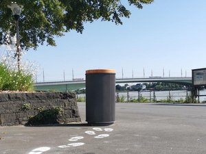 Öffentlicher Papierkorb von bonnorange an der Rheinpromenade mit Blick auf die Kennedybrücke.