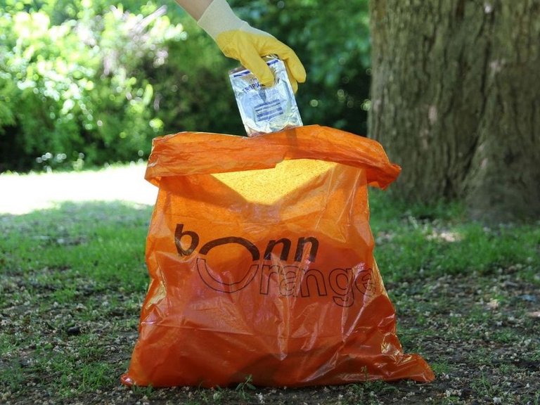 Sauberkeitsaktionen von bonnorange Orangener Müllsack von bonnorange, eine Hand legt Abfall hinein.