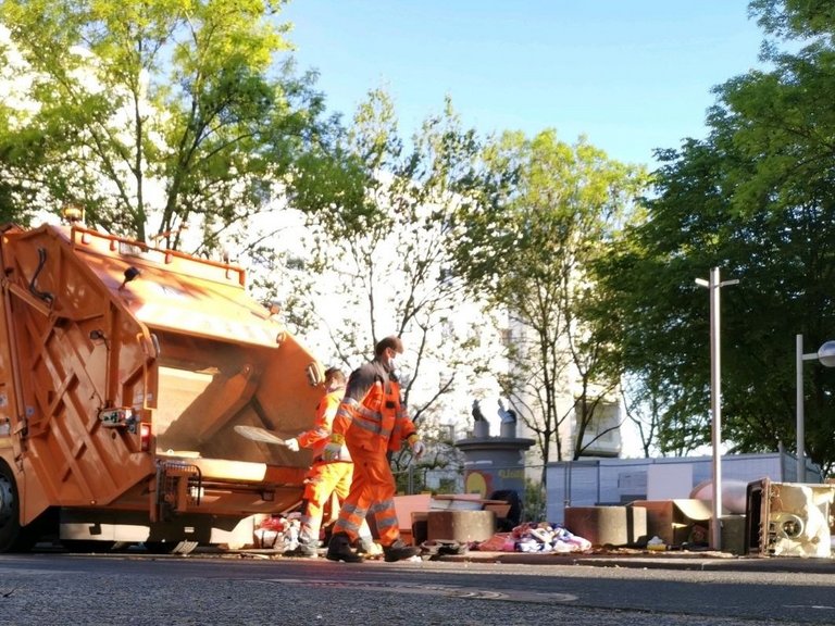 Abfallsammelfahrzeug mit zwei bonnorange-Mitarbeitern, die Sperrmüll einladen. 