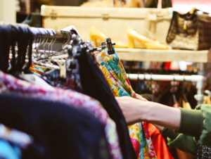 Hand greift nach Kleidung auf einer Kleiderstange.