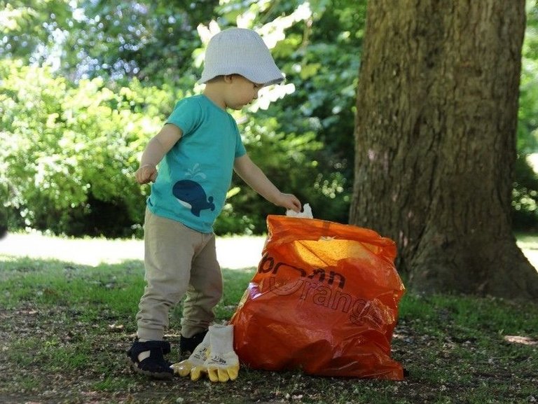 Bonn Picobello: ein kleiner Junge wirft Abfall in einen orangenen Müllsack