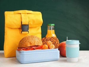 Schulranzen, Butterbrotdose mit Brötchen, Saft, Apfel und Mehrwegbecher für unterwegs