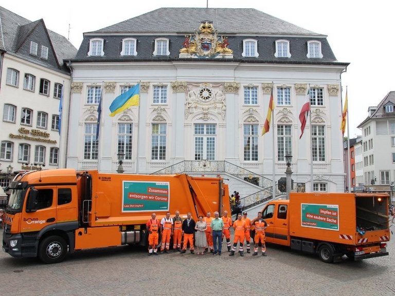 Zwei Fahrzeuge von bonnorange mit der aktuellen Impfkampagne der Stadt Bonn vor dem Alten Rathaus
